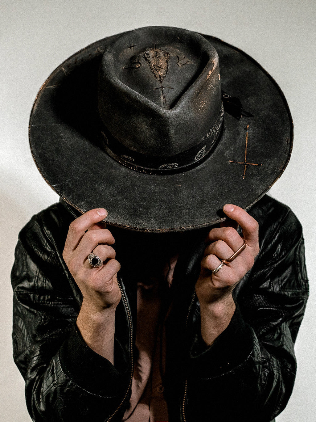 Model wearing a dark black burned hat in a leather jacket with a white background.