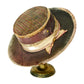 A vintage-style wide-brim hat displayed on a small gold stand against a plain white background. The hat features a dark brown brim, a gold-and-purple patterned crown, and a cream ribbon with a gold button and bow.
