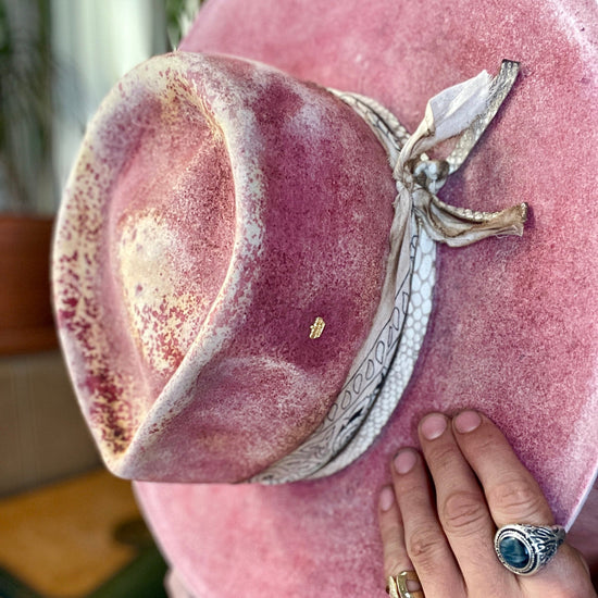 Pink velvet custom made hat with a ribbon held by a hand wearing a gold ring.