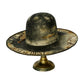 A distressed, vintage-style black and beige sombrero hat displayed on a gold-colored metal stand against a plain white background.