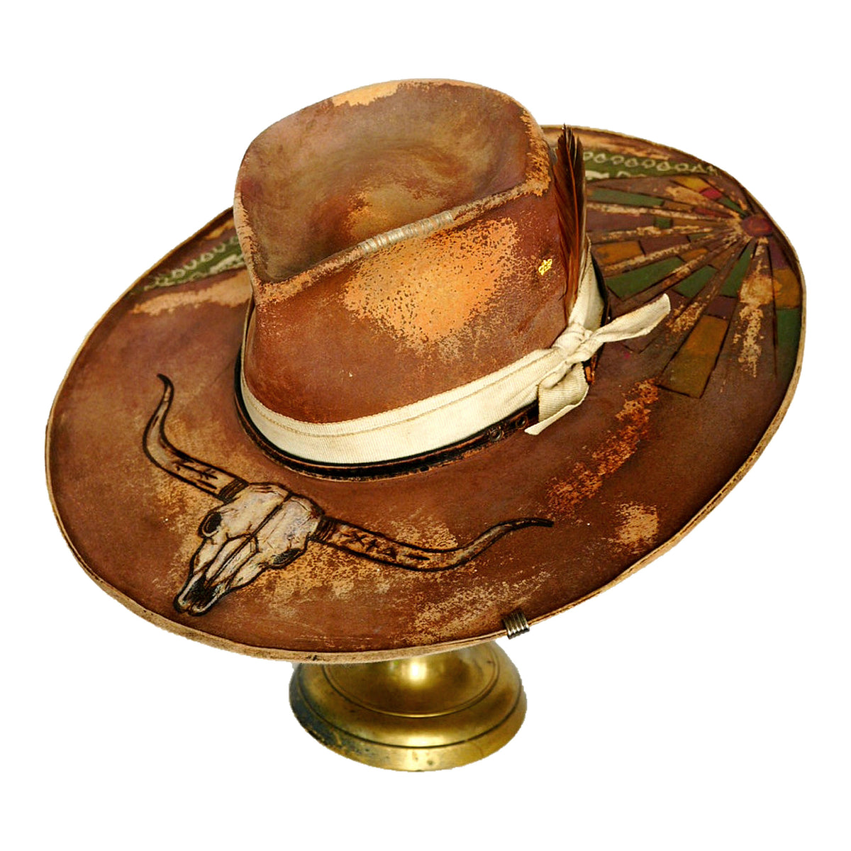 A distressed brown cowboy hat with a cream ribbon band and western-style painted details, displayed on a gold-colored stand against a white background.
